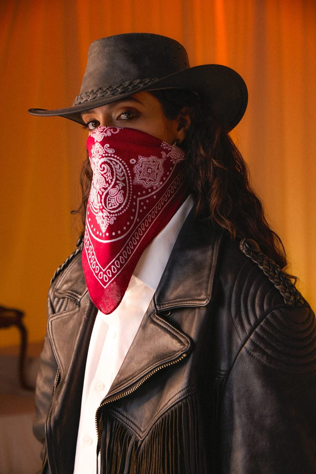Woman in cowboy hat, face mask, and leather jacket.