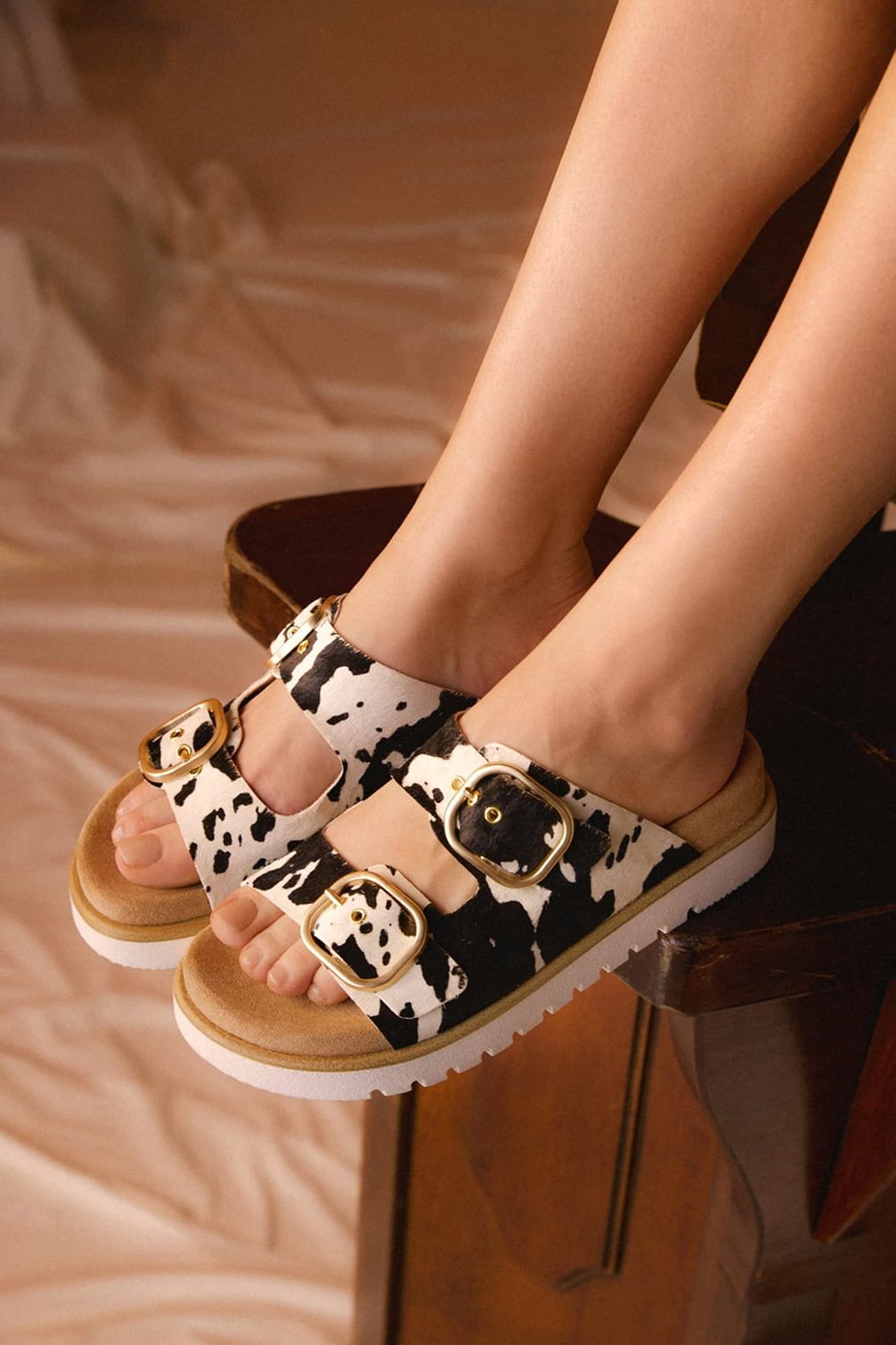 Cow print sandals with gold buckles on feet