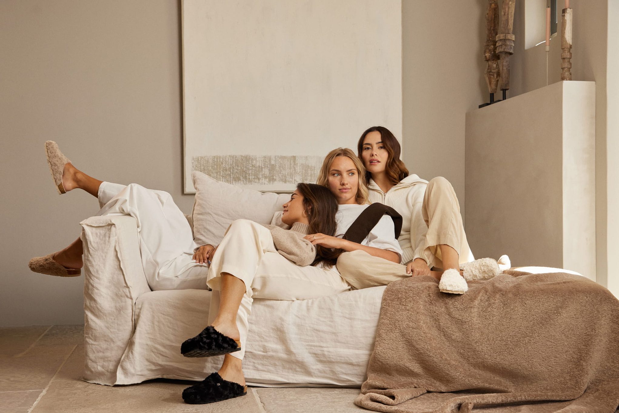 Three women relaxing on a couch, dressed casually.