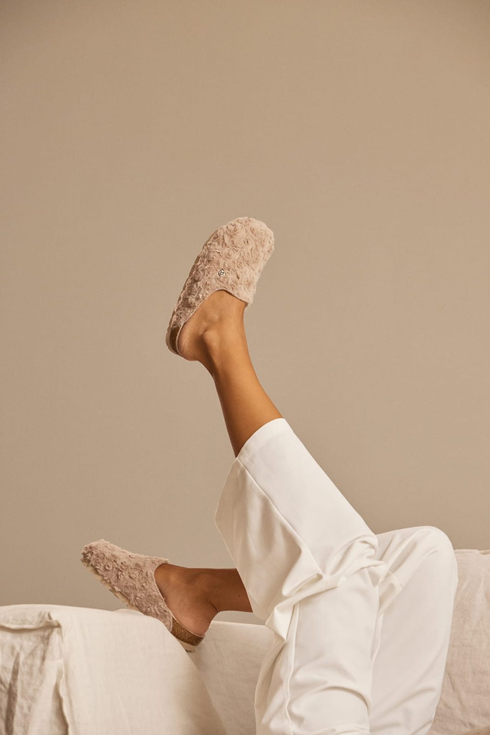 Fuzzy slippers on a leg with white pants.