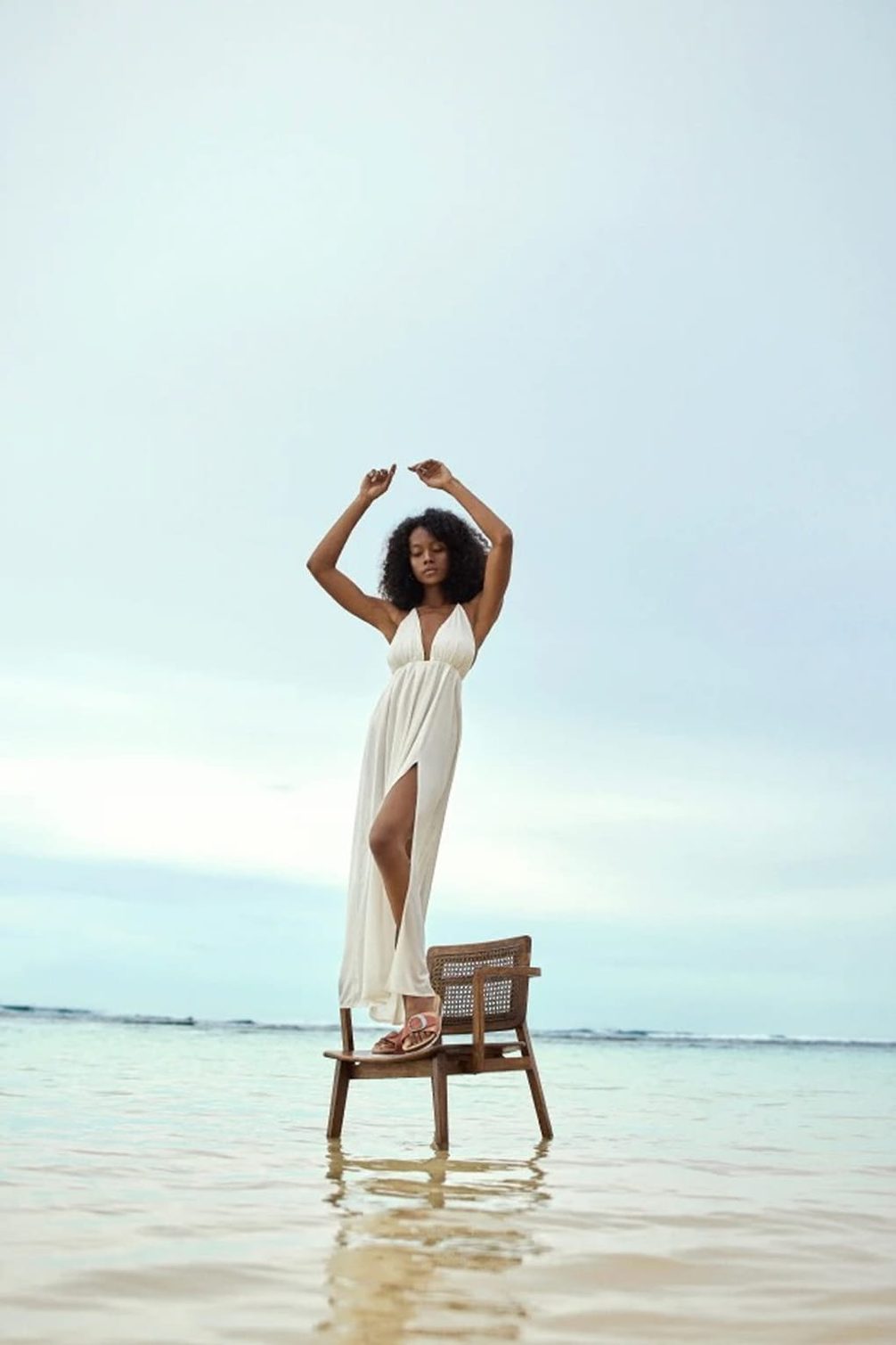 Model in white dress stands on chair in water
