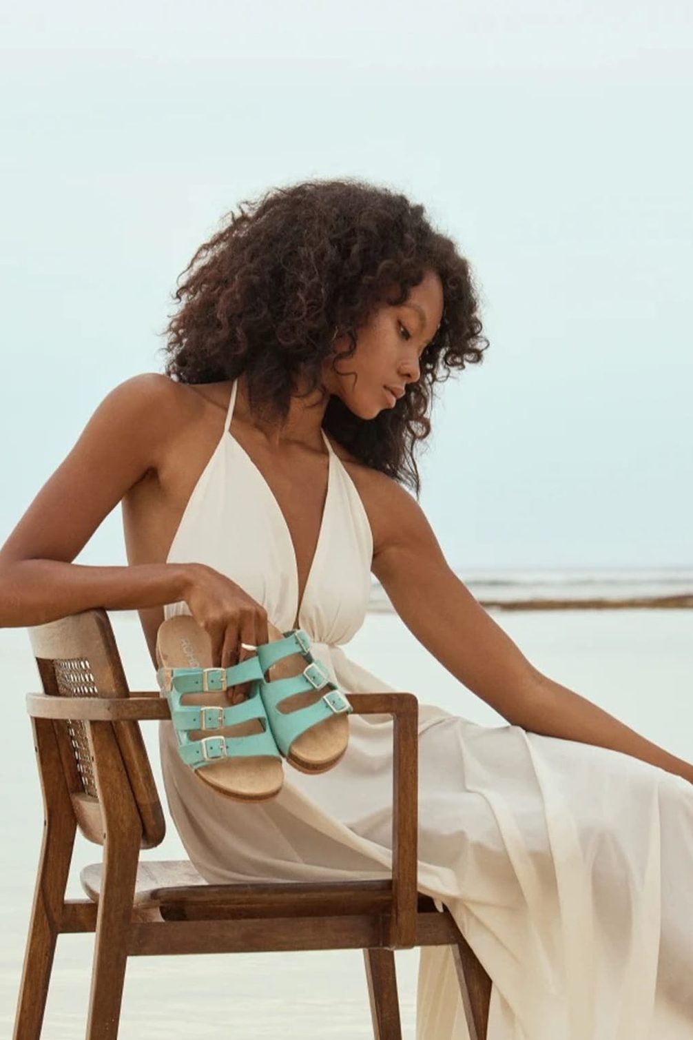 Light aqua sandals held by a woman on chair.