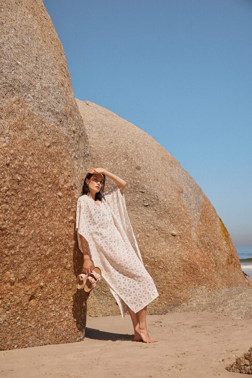 Woman in caftan on beach near rocks