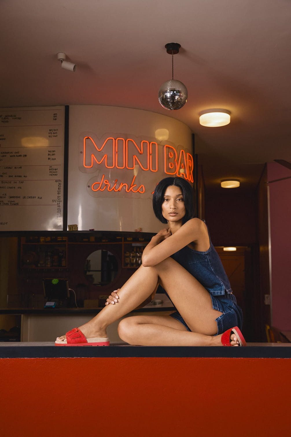 Woman sitting in front of "Mini Bar" sign near a disco ball.
