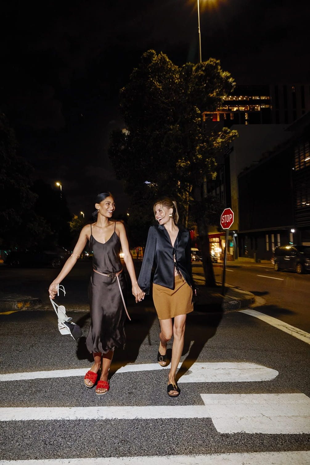 Two women cross a street at night
