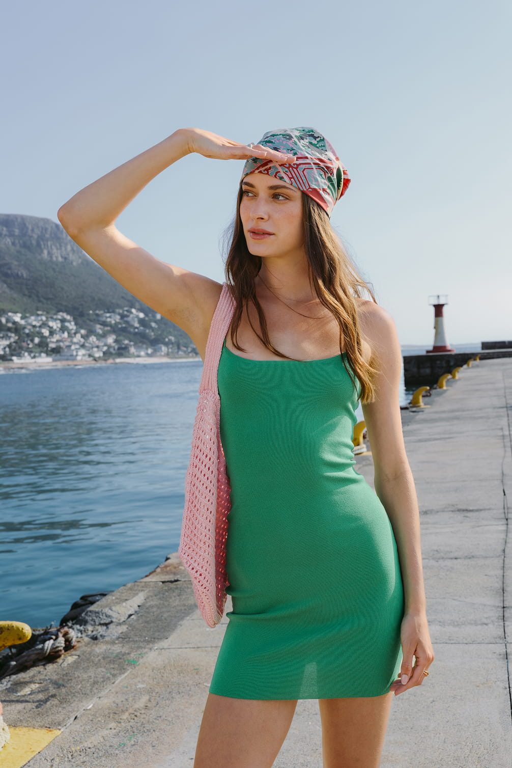 Woman in green dress and headscarf looking out at sea.