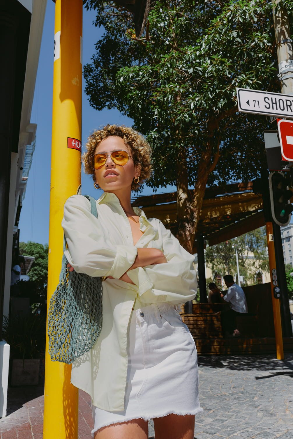 Woman in yellow shirt and white skirt with sunglasses.