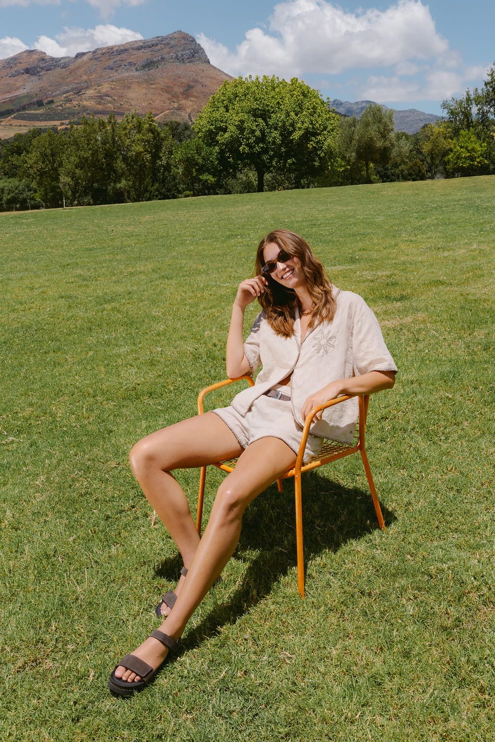 Woman in shorts and linen shirt sits in a chair outdoors.