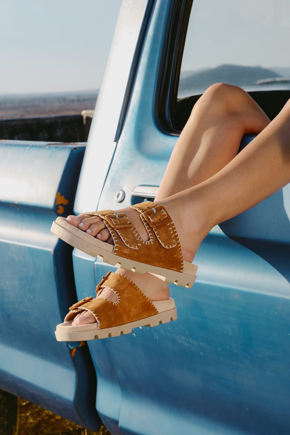 Brown sandals on feet by a blue truck