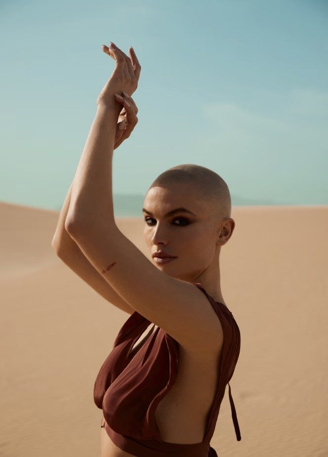 Bald woman with arms raised in desert landscape