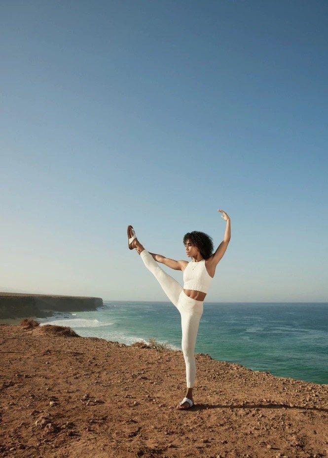 Woman in white performs yoga pose by ocean