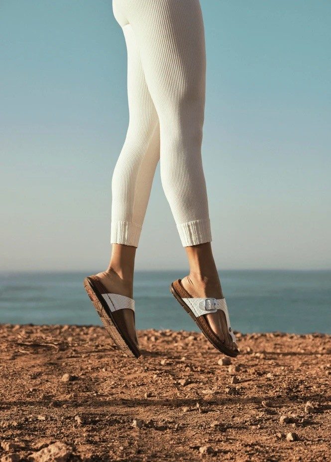 Legs in white leggings and sandals jumping over rocky ground