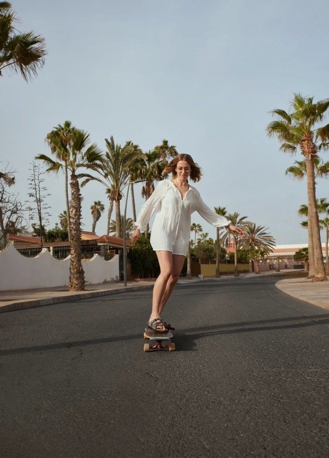 Woman skateboarding down a street with palm trees